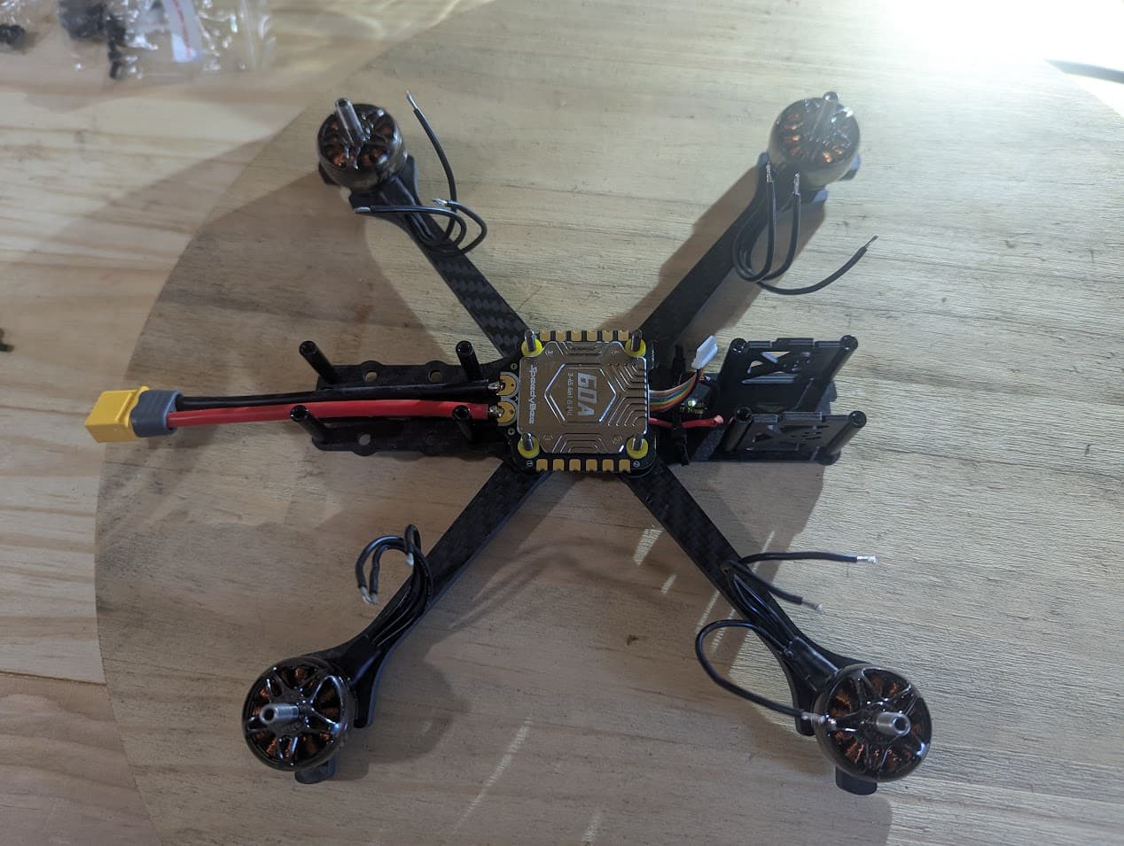 Top-down progress photograph of the Source One V5 frame with motors mounted, loose motor leads, exposed SpeedyBee stack and XT60 power lead