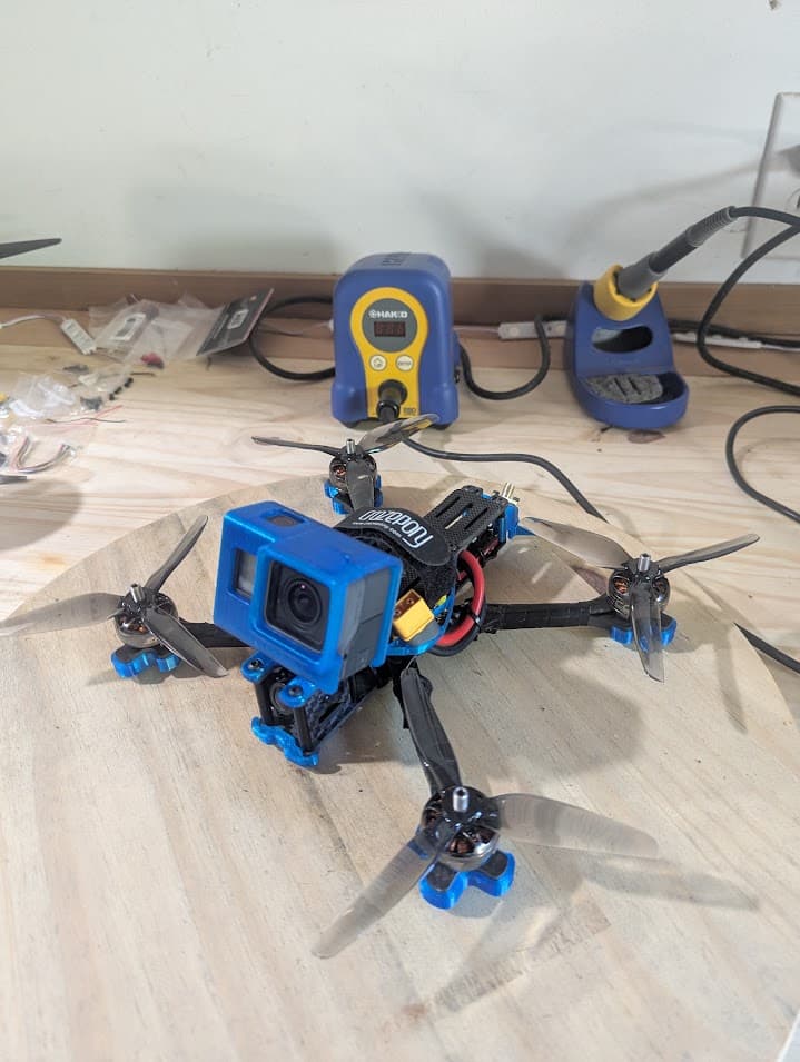 Assembled Source One V5 on the workbench with propellers, battery strap and an early blue printed GoPro mount